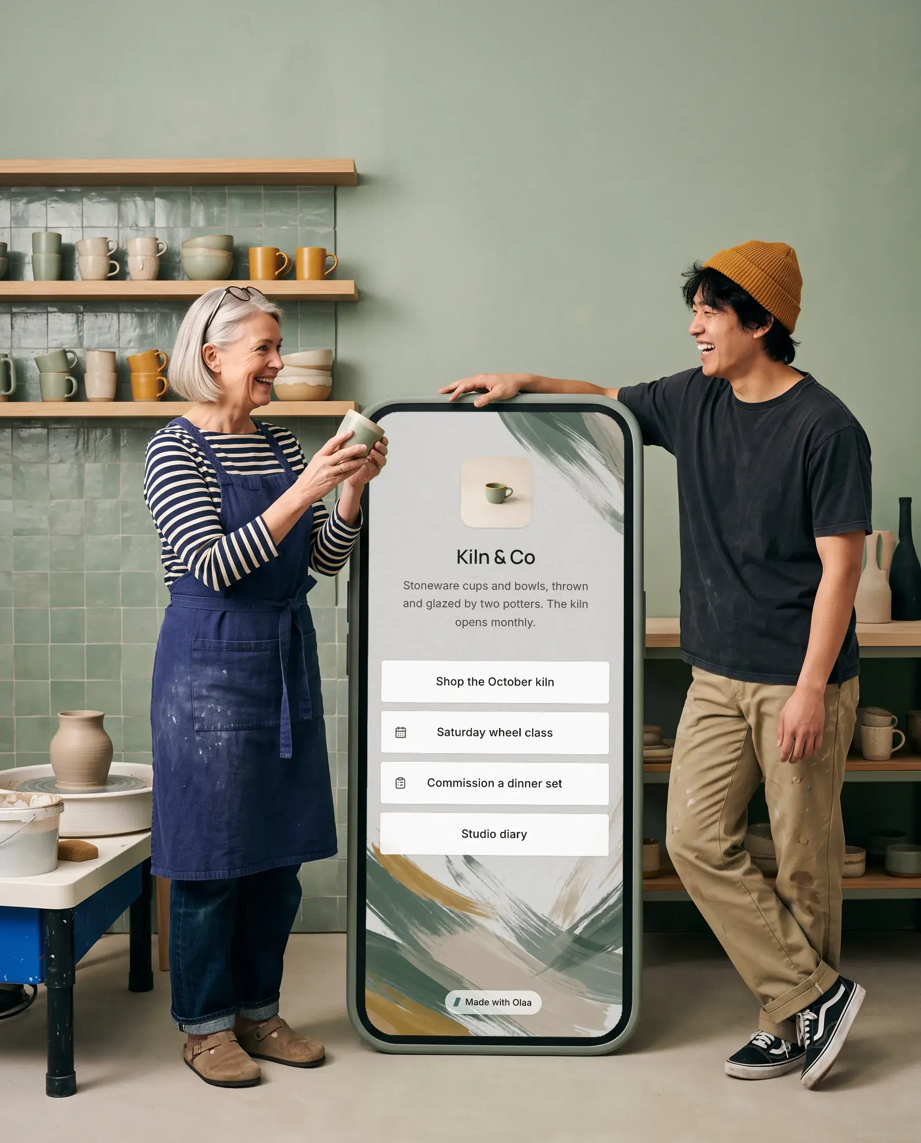 Ingrid and Theo of Kiln & Co beside a giant phone showing their Olaa page