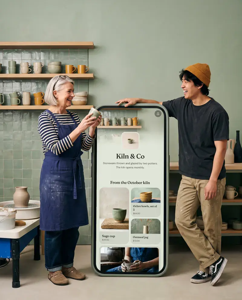Ingrid and Theo of Kiln & Co. beside a giant phone showing the studio’s Olaa page