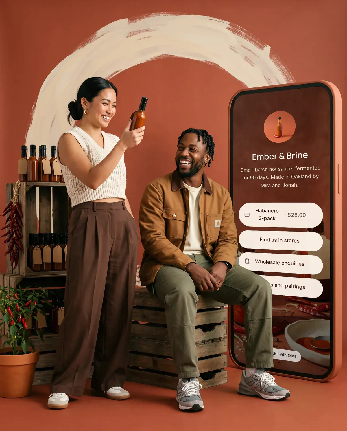 Mira and Jonah, founders of Ember & Brine. Beside them stands a giant phone showing their Olaa page.