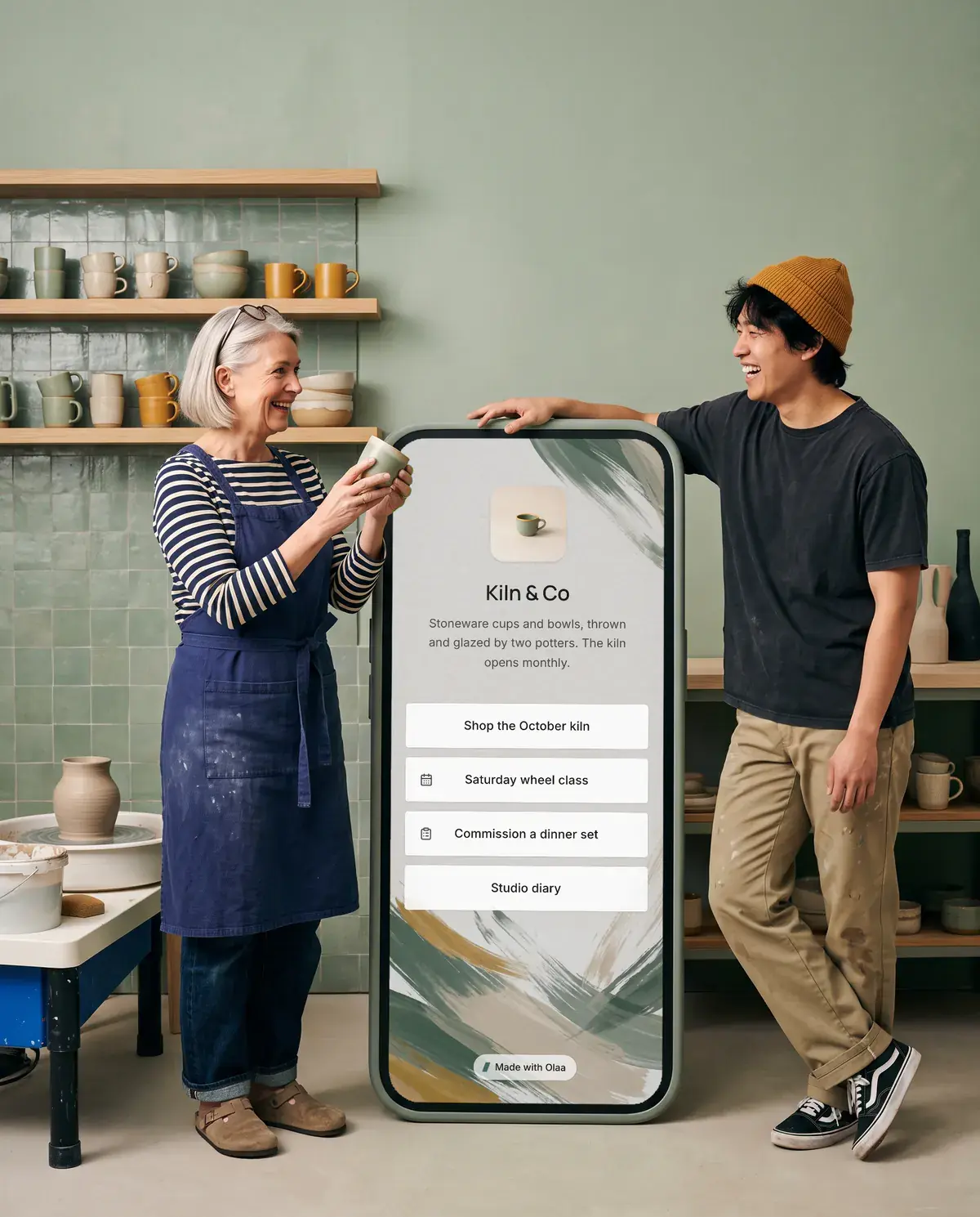 Ingrid and Theo of Kiln & Co. Beside them stands a giant phone showing their Olaa page.