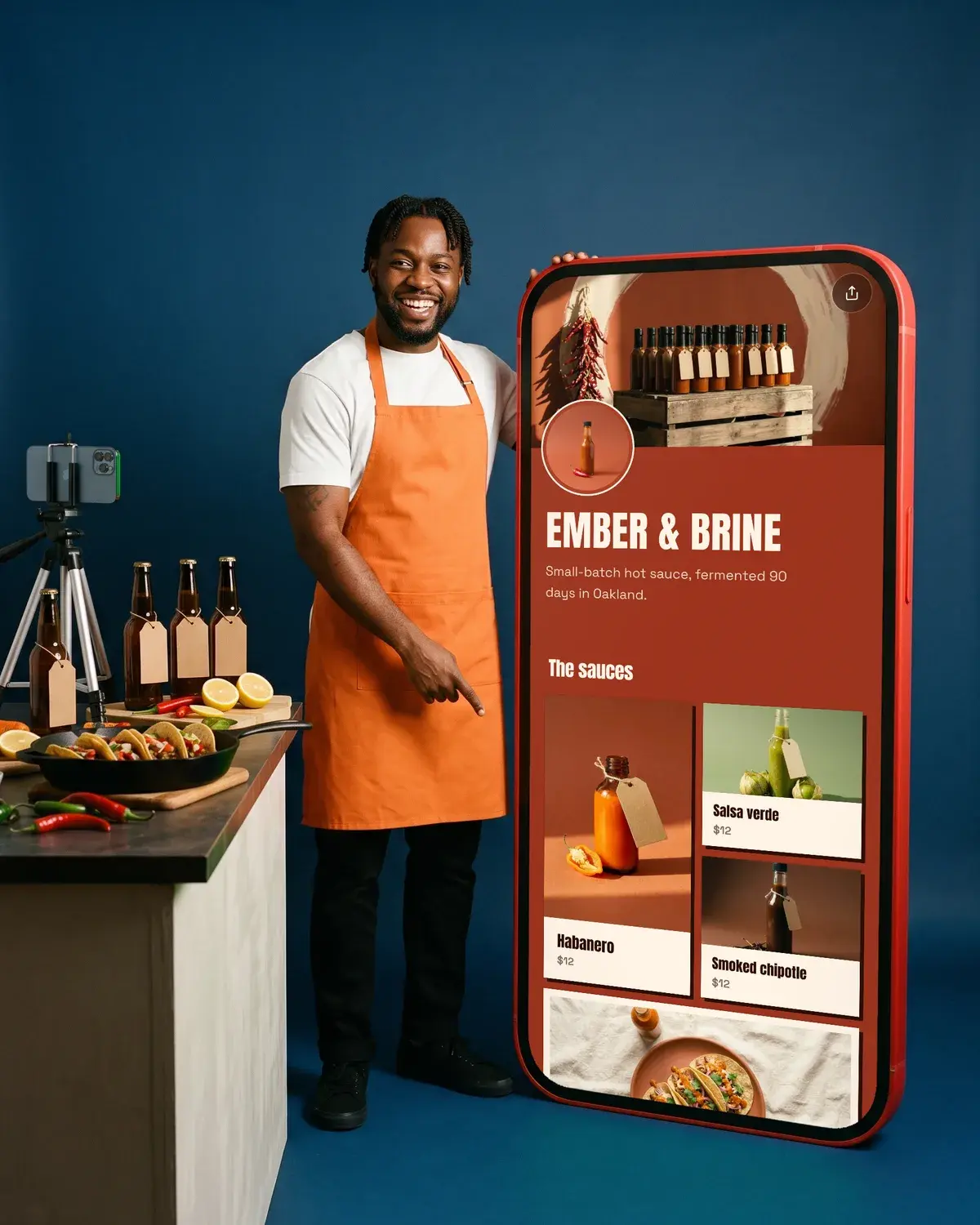 A cook points down at his counter of tacos beside a giant phone showing the Ember & Brine page