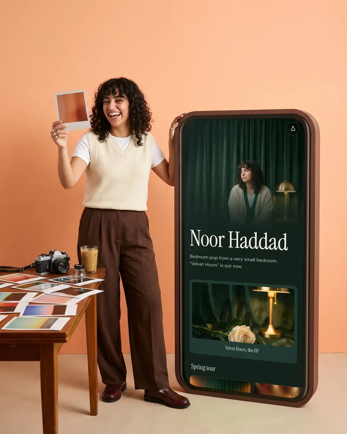 A musician holds up a film print on a peach set beside a giant phone showing her music page